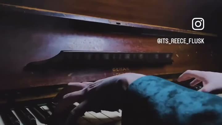 Hands play an old upright piano in warm low light.