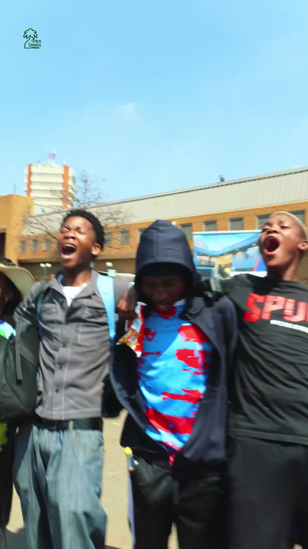 Students cheer with their arms around each other on a sunny city street.
