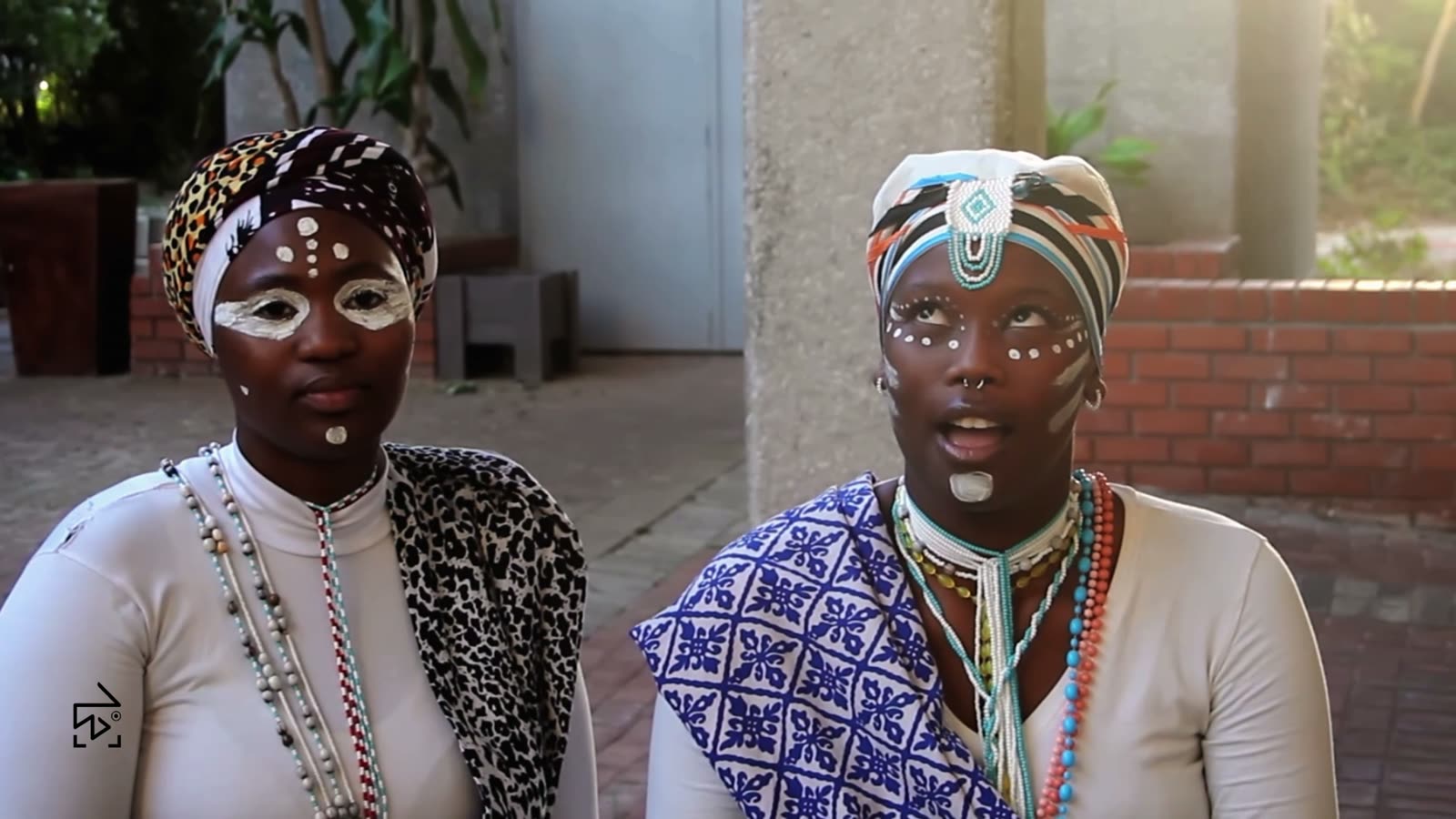 Two young women in traditional Xhosa dress and white face paint, beaded necklaces at their throats.